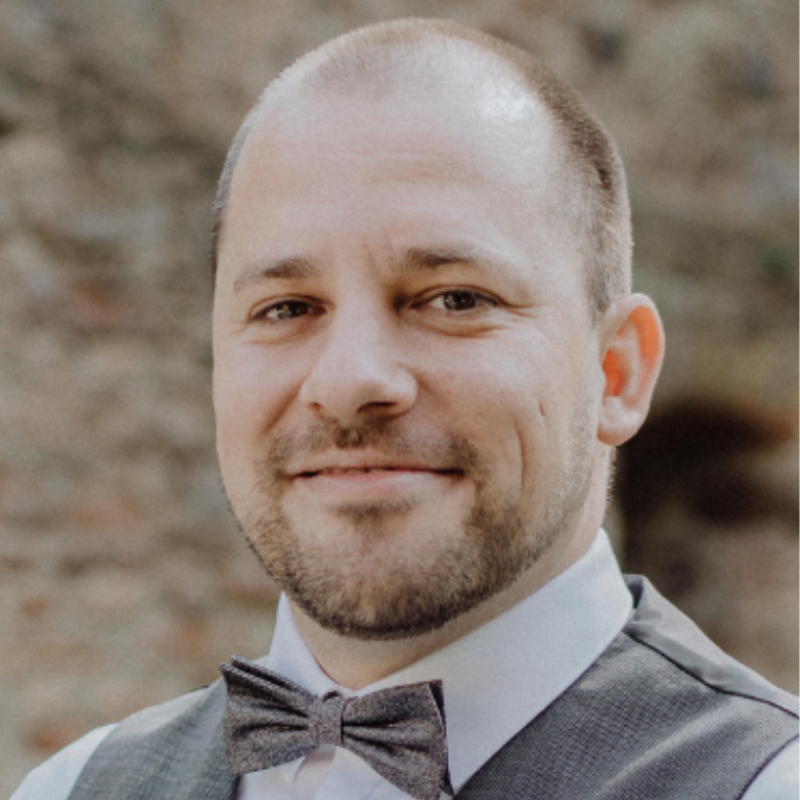 Ein lächelnder man mit Bart im Anzug.