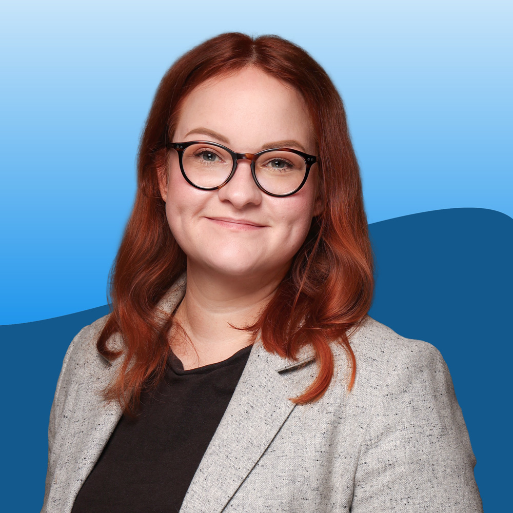 Pressefoto von einer rothaarigen Frau mit Brille und Blazer.