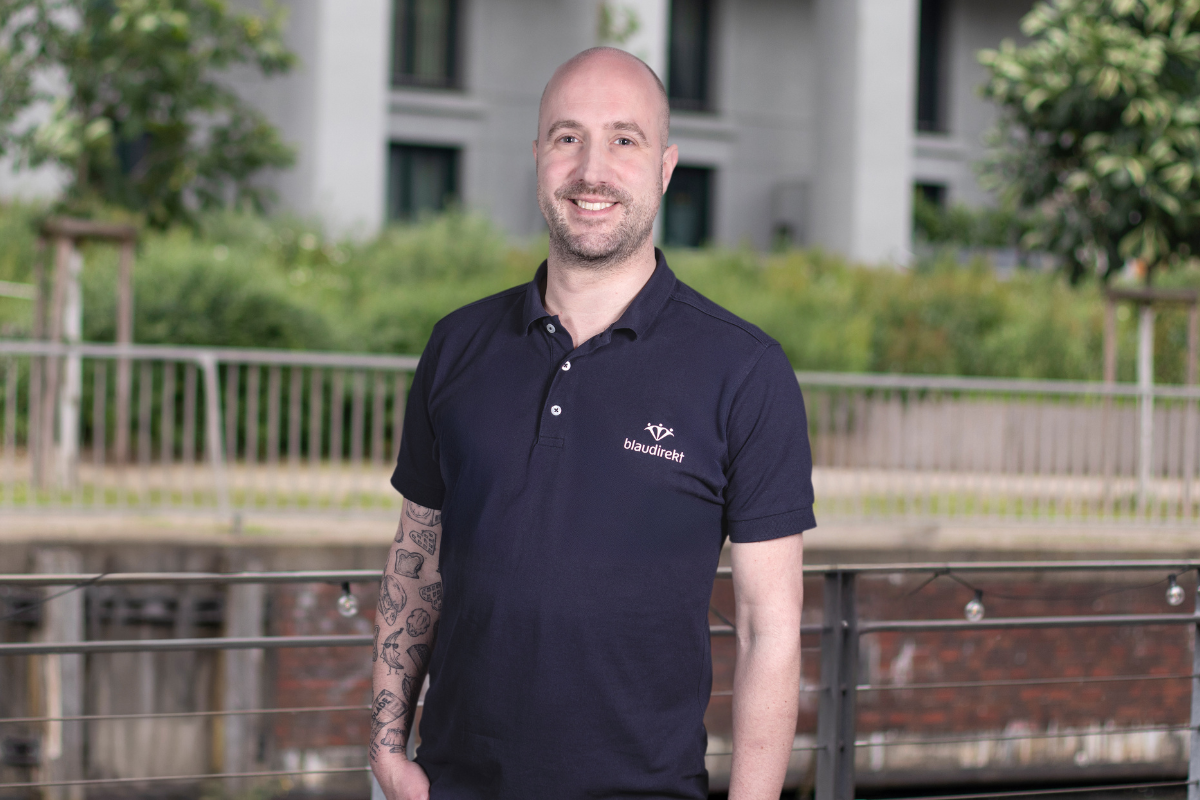 Mann im blau direkt Poloshirt lächelt in die Kamera.