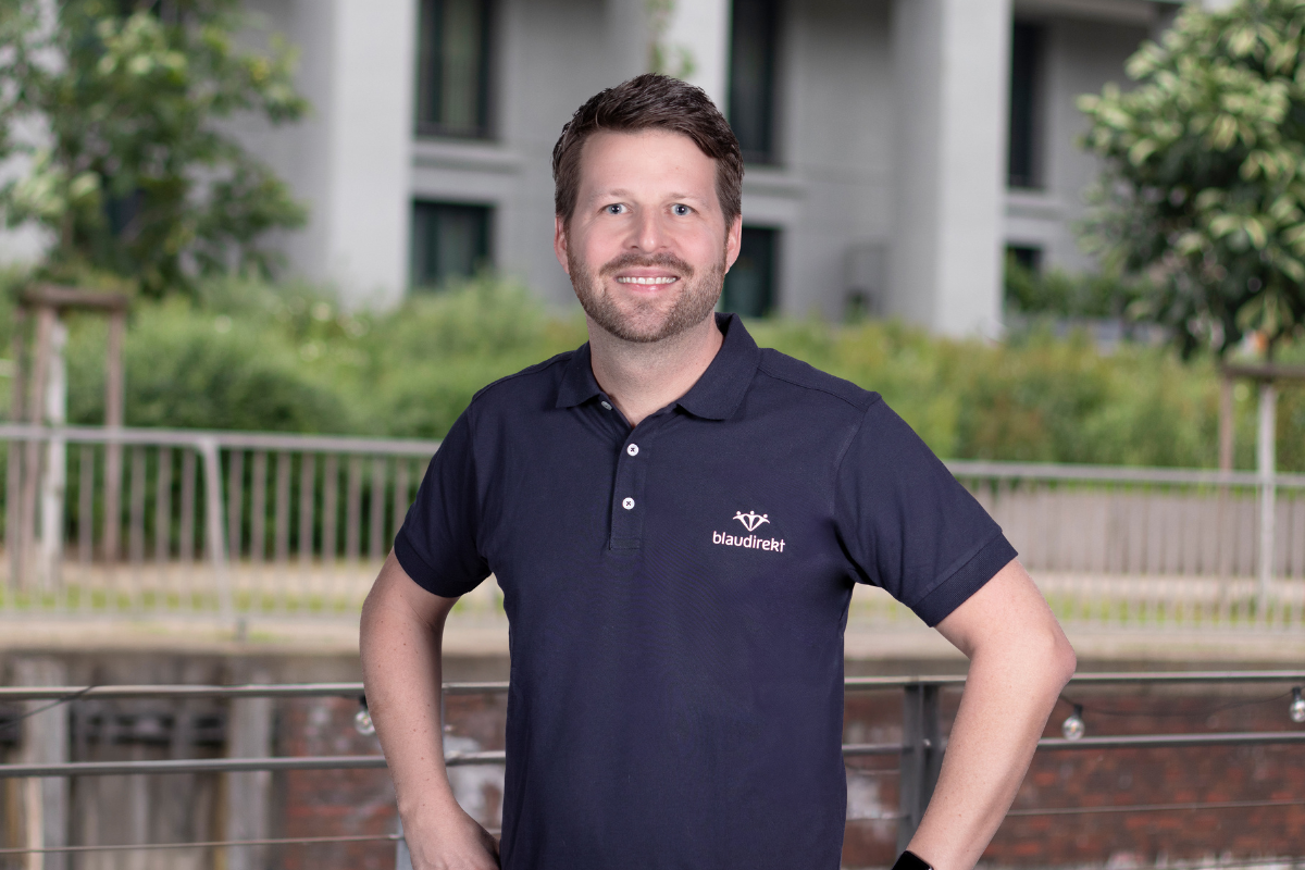 Braunhaariger Mann im blau direkt Poloshirt lächelt in die Kamera