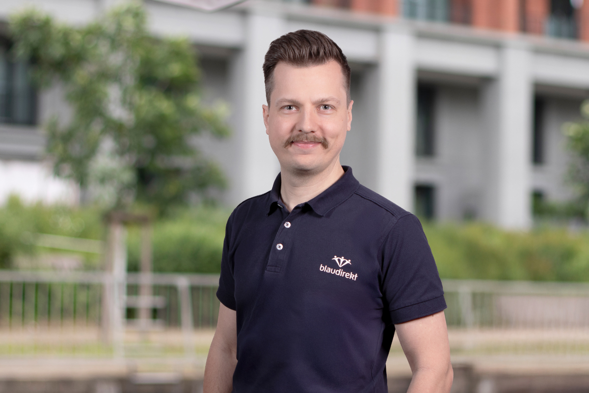 Braunhaariger Mann im blau direkt Poloshirt lächelt in die Kamera